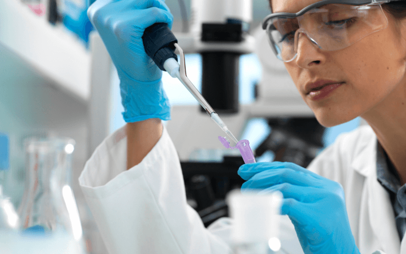 Bir laboratuvar teknisyeni, pipetle numune alıyor. Detaylı ve dikkatli çalışma ortamı.